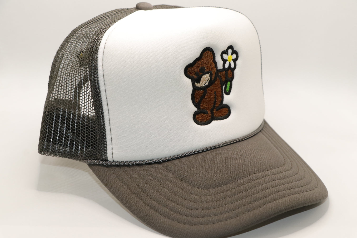 White Front Panel with a Charcoal mesh back and Charcoal brim with a Brown Bear holding a Magnolia Daisy